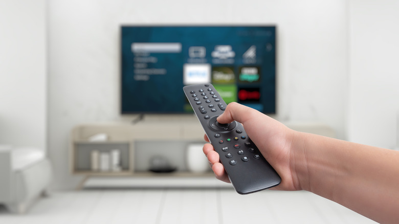Man holding remote and pointing towards a blurred out smart tv