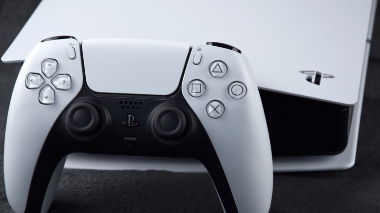 A PS5 DualSense controller leaning against a PlayStation 5 system