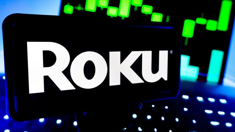 Roku logo is displayed on a screen with stock market performance chart in the background