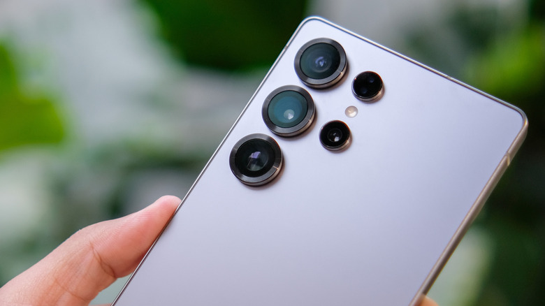 An individual holds a silver Samsung Galaxy device in their left hand, the backside of the device shows its multiple cameras