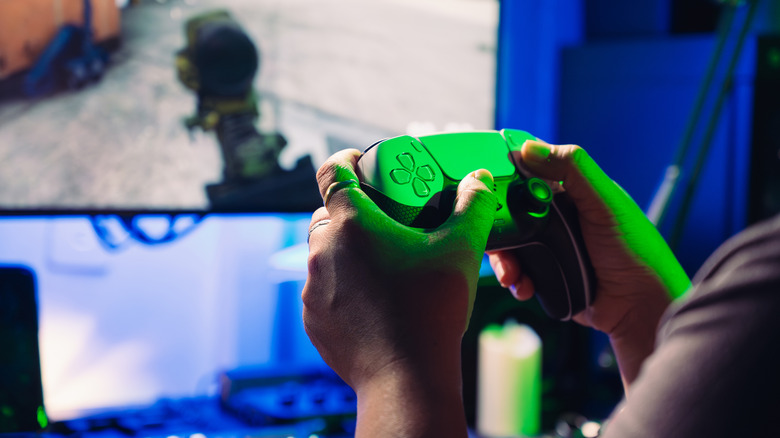 A person playing a game on their TV while holding a DualSense bathed in green light