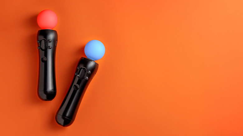 Two PlayStation Move controllers, one with a red LED and another with a blue LED, on an orange surface