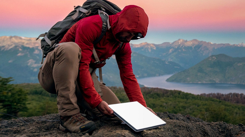 Hiker wearing red hoodie placing Starlink Mini dish on a rock