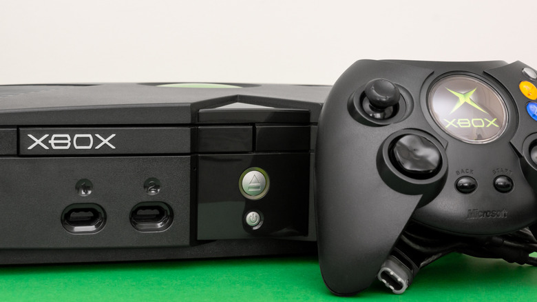The original Xbox next to the Duke controller on a green and white background