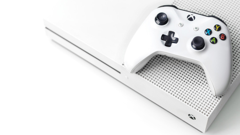 White Xbox One with a controller on top of the console on a white background