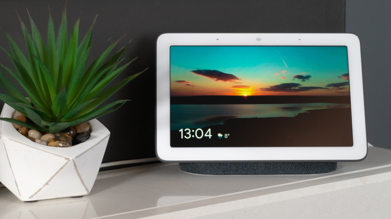 a Google Nest Hub sitting on a desk next to a plant