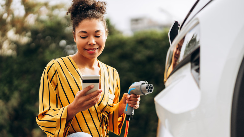 A woman looks at her phone while charging an electric vehicle.