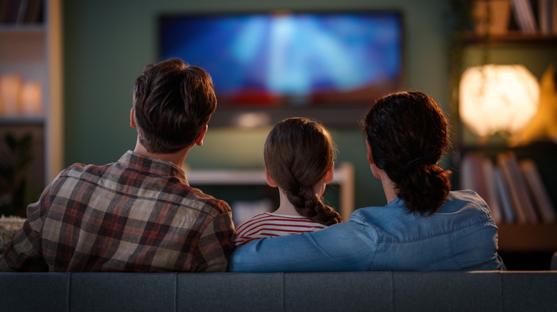 A family sitting on a couch and watching a movie in their living room