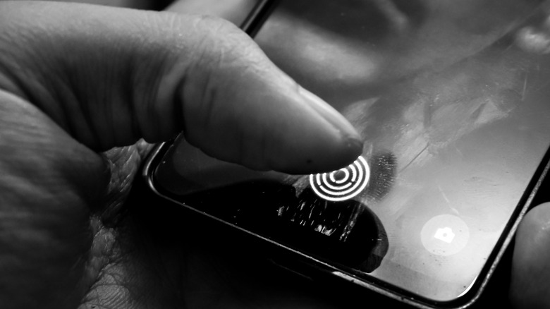 A person's thumb about to press a fingerprint scanner on a phone