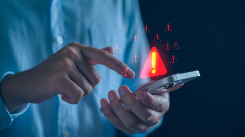 A man in a blue shirt taps on his phone screen, over where hover a series of red caution icons.