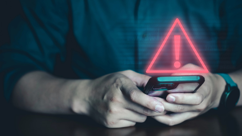 A red scam icon projects from a phone screen as a faceless man types.