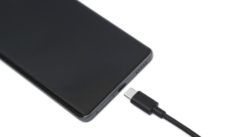 A black smartphone with  a charger cord being inserted into it using a USB-C connector