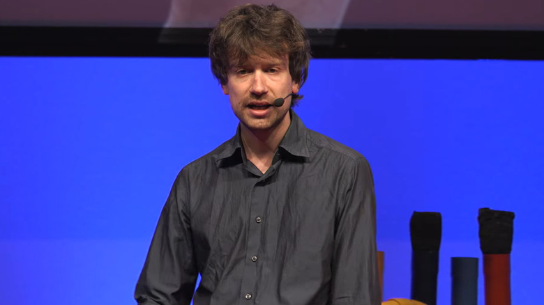 Michele Spagnuolo, wearing a dark button up shirt and microphone, gives a Ted Talk before a blue background