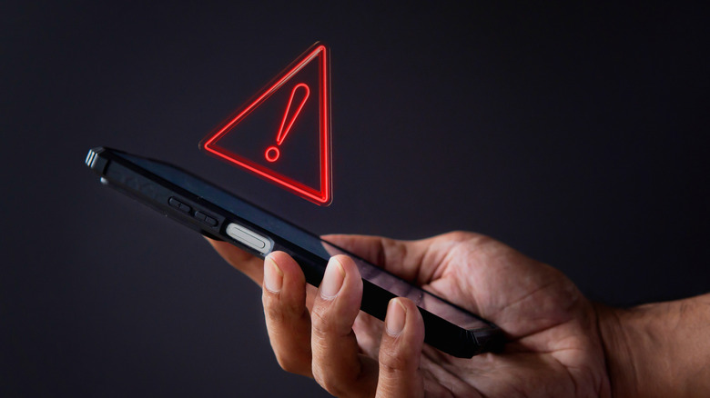 close-up hand holding smartphone with warning sign concept above