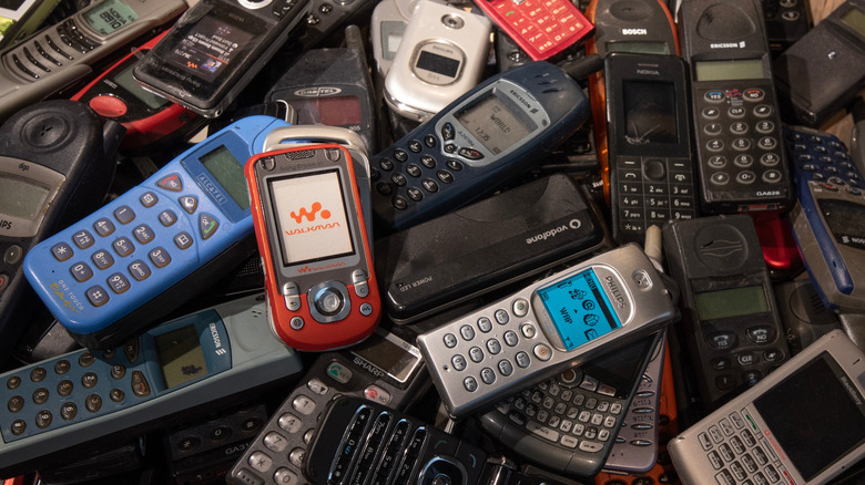 A collection of old keypad phones, and a digital Walkman, in a pile.