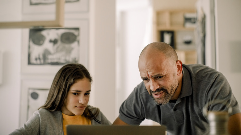 teenage girl and father look at her laptop