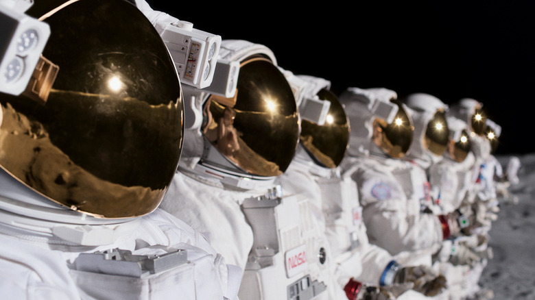 Several astronauts in full spacesuits standing in a line on the moon.