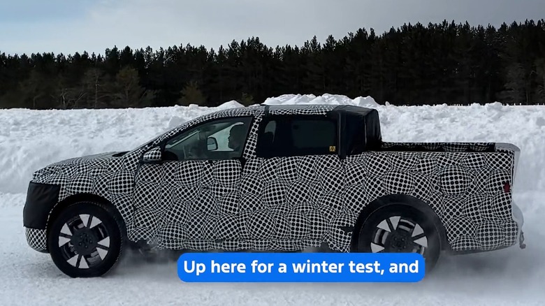A side view of Ford's newest electric truck, the truck itself is covered in a wrap that camouflages its design, and the vehicle is driving through heavy snow