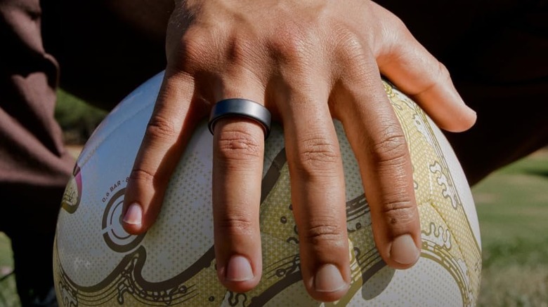 A person wearing the Oura Ring 4 smart ring on their finger while holding a ball.