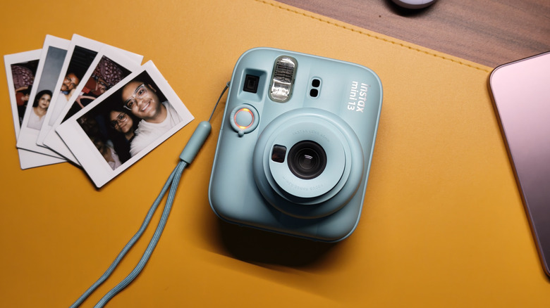 Fujifilm Instax Mini 13 kept on a yellow desk mat with it's images on the left