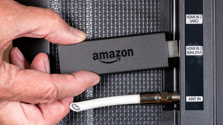 A person connecting an Amazon Fire TV Stick to a smart TV.