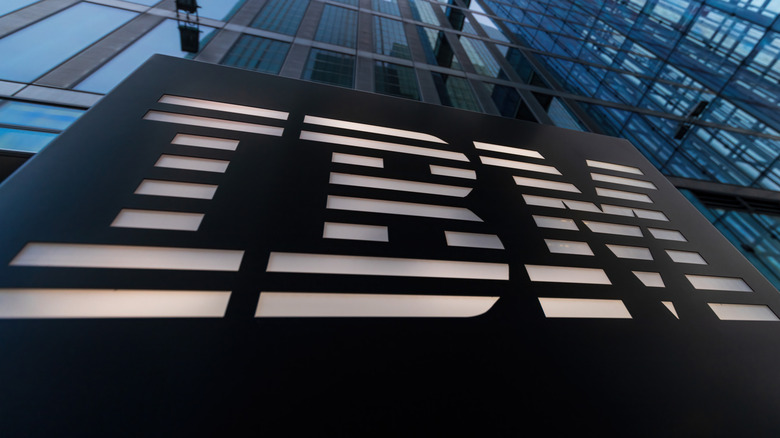 A low-angle view of an IBM logo sign in front of a modern glass office building.