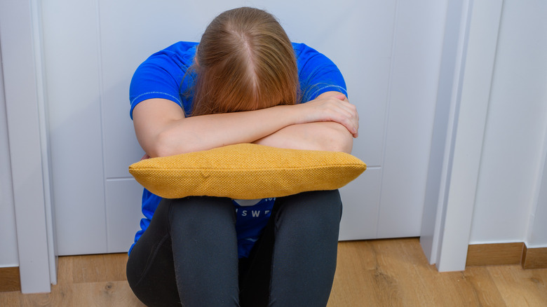 a woman cries into a pillow while sitting against a door