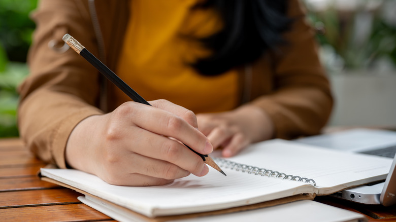 a woman writing by hand with a pencil in a notebook