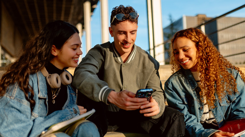Three young people gathered around a smartphone