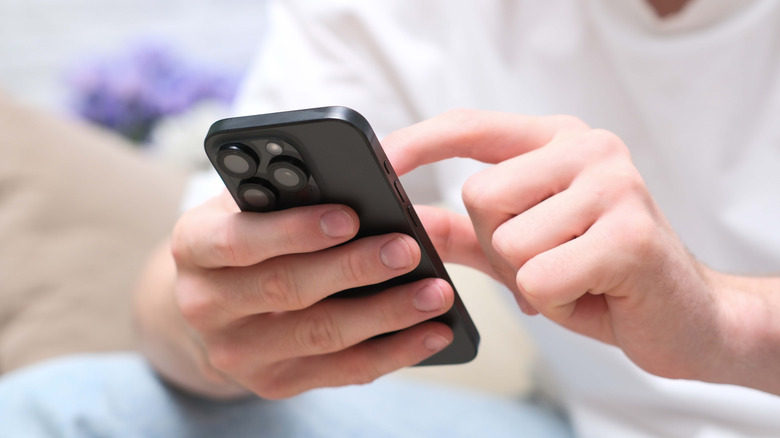 A close up of a man in a white shirt holding a black iPhone