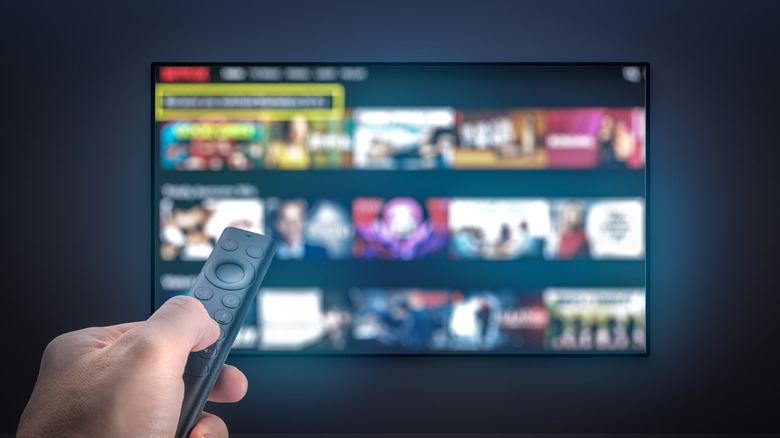 hand holding a remote control, tv on the wall in the background