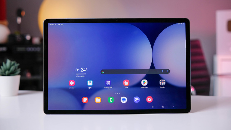 An Android tablet is perched on top of a table. The home screen shows several apps.