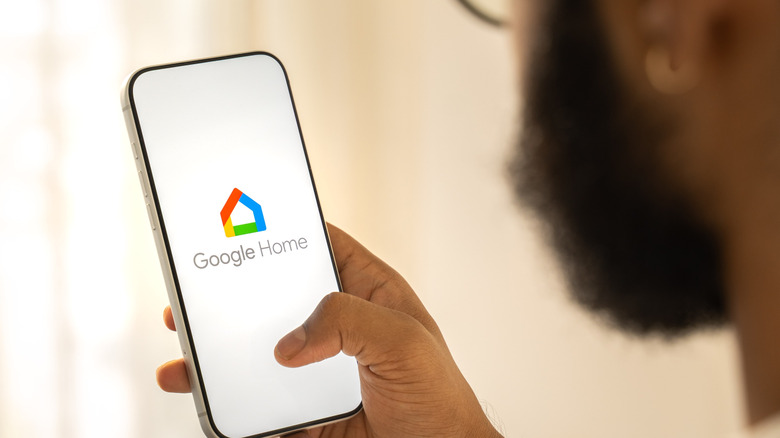 A person holding a smartphone with the Google Home logo visible on it
