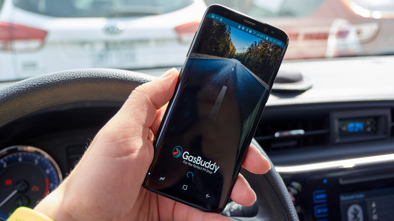 GasBuddy app on screen of phone held in hand of person inside car