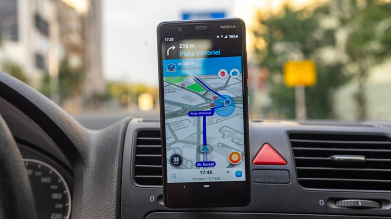 Waze open on a smartphone that hangs from a connector in a car with directions pulled up