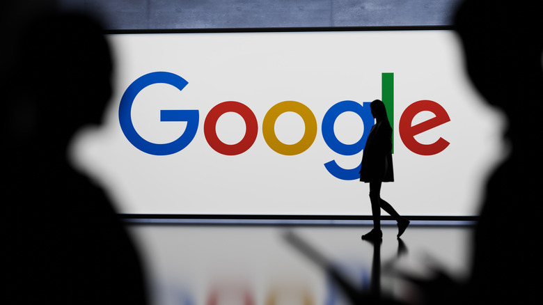 A Google billboard in the background, with people walking in front of it.