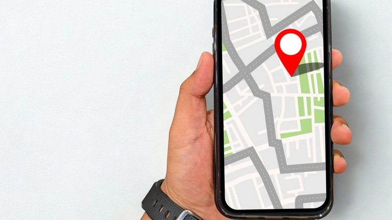 concept for location sharing on map, hand holding smartphone showing map and red location marker