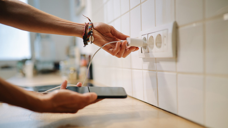 person plugging a smartphone charger into the wall to charge their phone