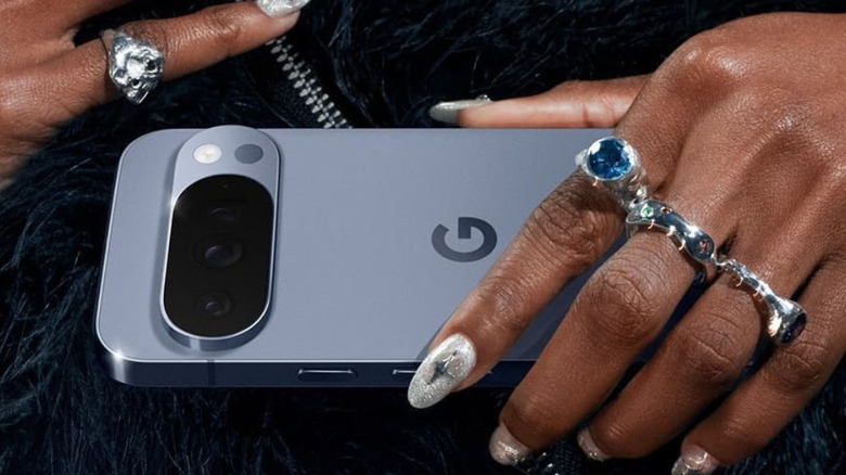 A Close up picture of a woman holding a Google Pixel 10 to her chest, showing hands with many sparkly rings.