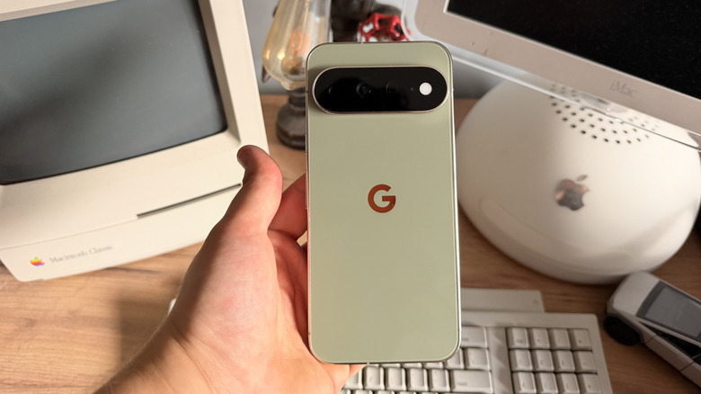 Pixel 11 Pro XL being held in hand above desk with vintage computers