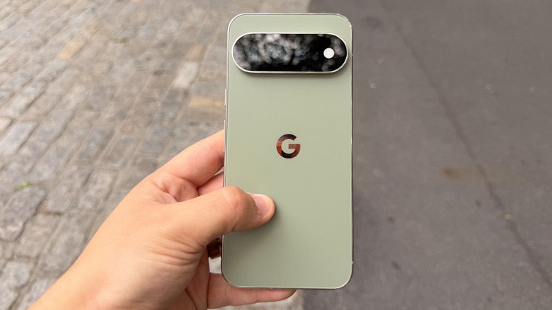 Holding the Pixel 11 Pro XL in one hand above two types of pavement