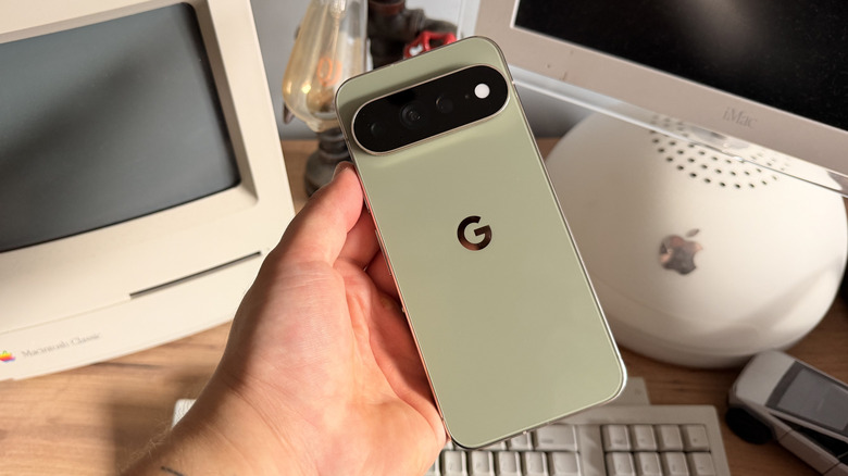 Pixel 11 Pro XL being held at an angle in hand above desk with vintage computers
