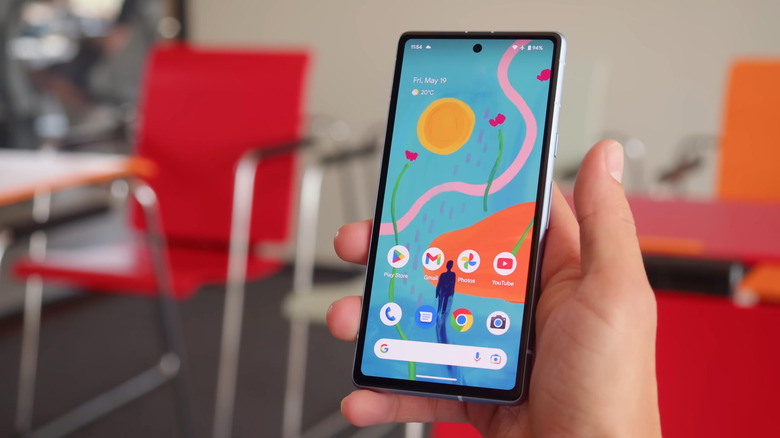 The Pixel 7a in hand with the home screen and Google search bar in view.