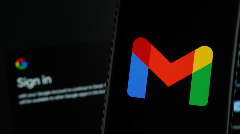 gmail logo on smartphone with computer screen showing google sign-in page in background