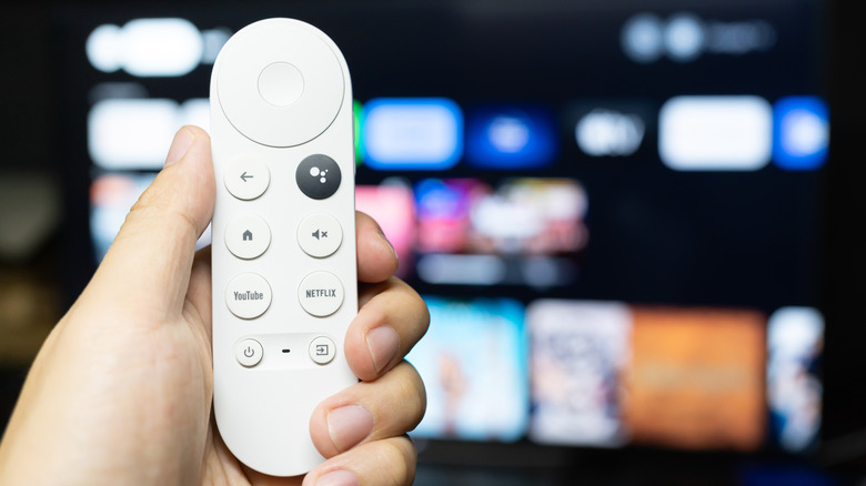 A person holding a Google TV remote against a blurred background