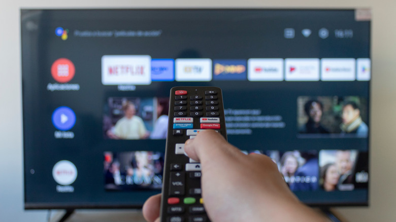 Person holding remote navigating Android TV interface on screen.