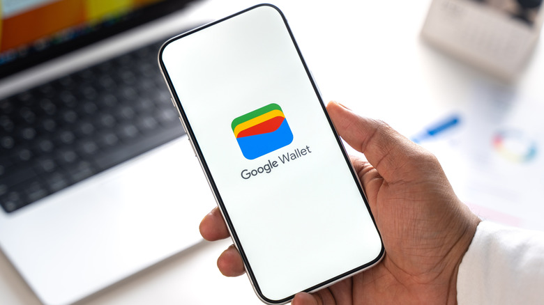 Image of the Google Wallet app logo on a smartphone screen in an office setting.