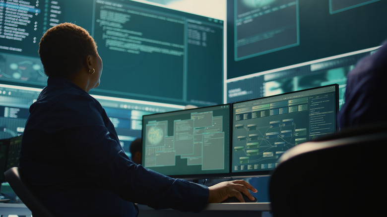 Person sitting at a desk surrounded by monitors showing technical information