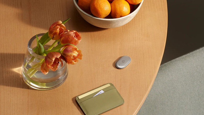 wallet and google pixel tag on a table next to a bowl of fruit and some flowers