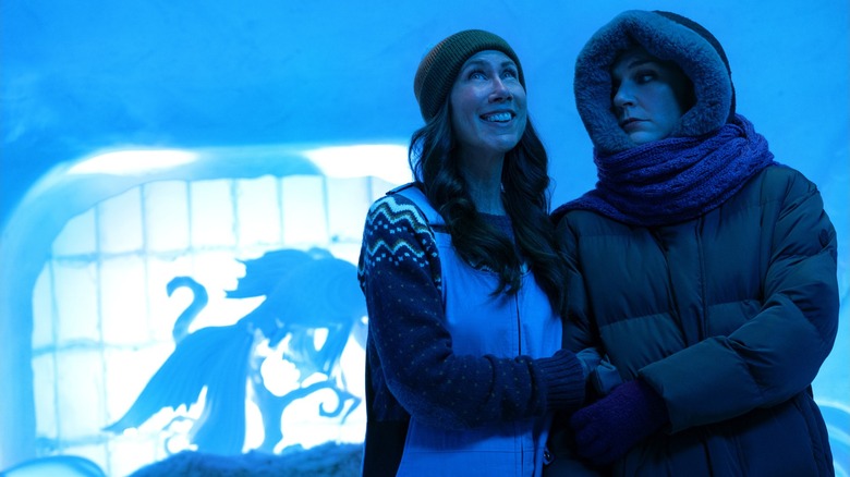An Apple TV promotional photo for the television series Pluribus, the image features Rhea Seehorn and Miriam Shor holding hands while they are heavily dressed inside of an ice hotel